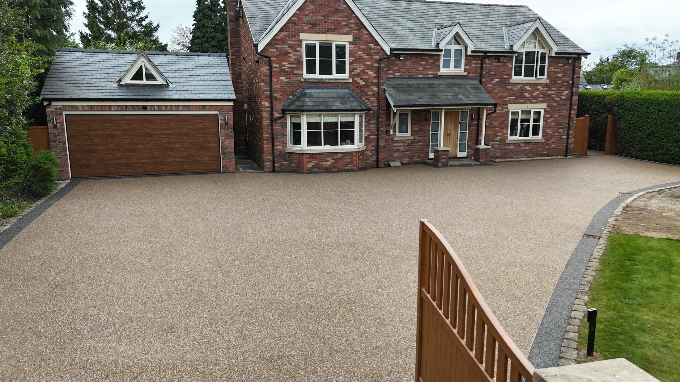 Warm resin driveway with a dark border outside a gated home