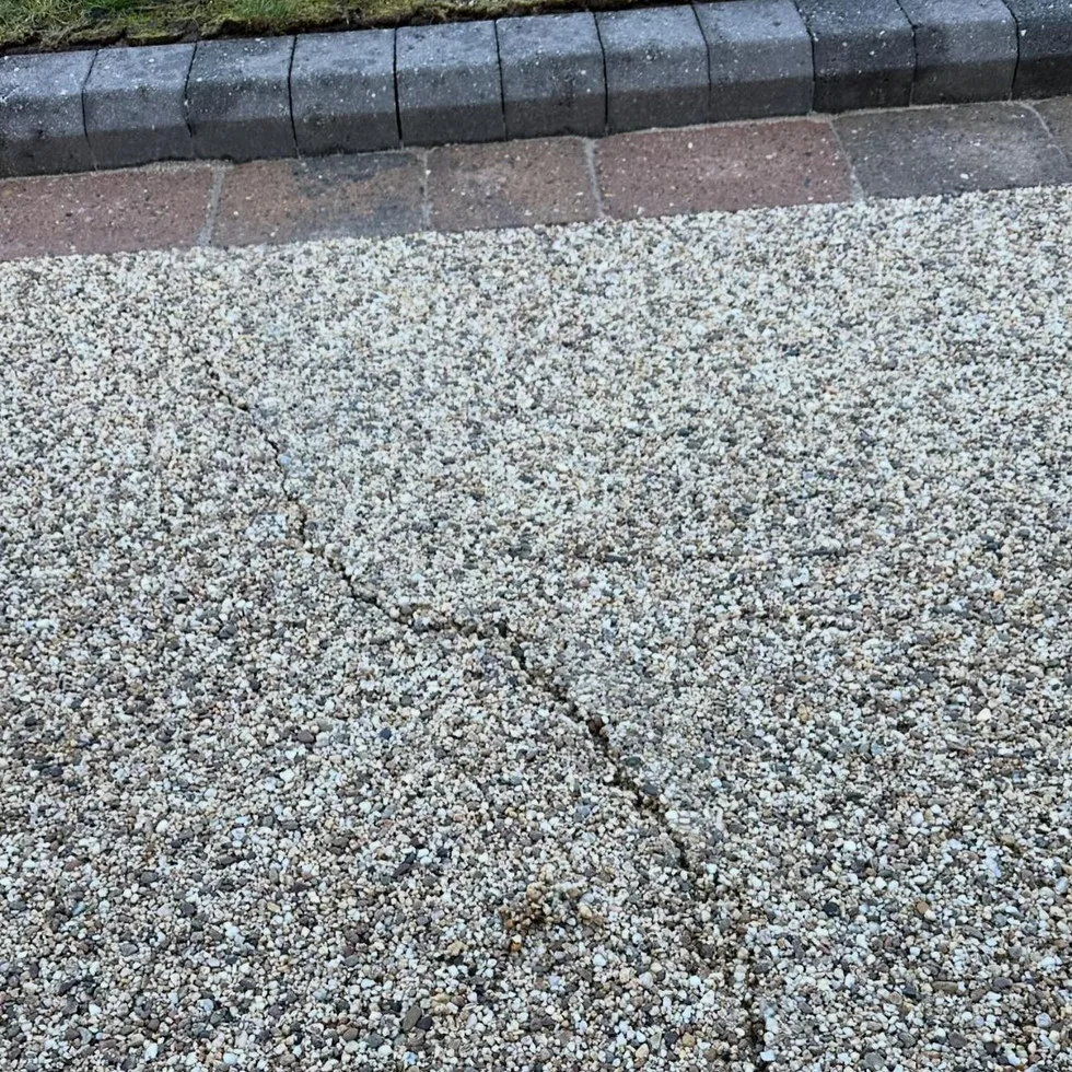 A genuine irregular crack running through a pale resin bound driveway surface