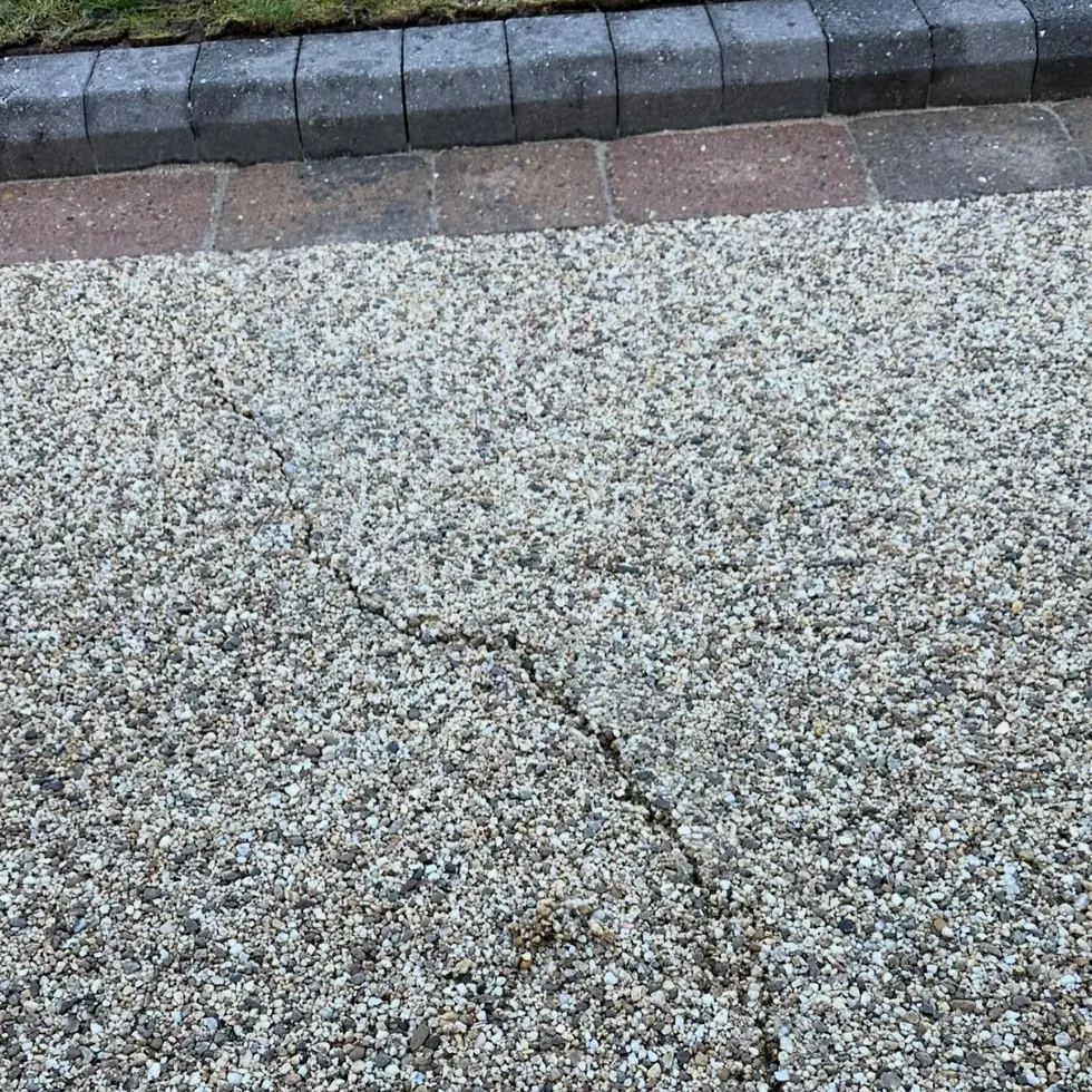 A genuine irregular crack running through a pale resin bound driveway surface